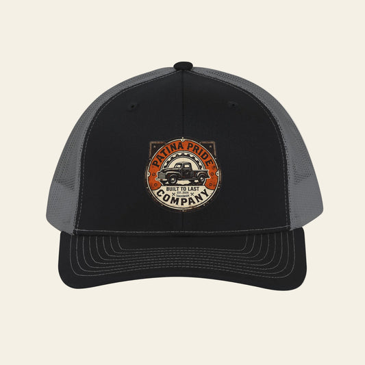 Grey snapback cap with the Patina Pride logo embroidered on a black front panel.